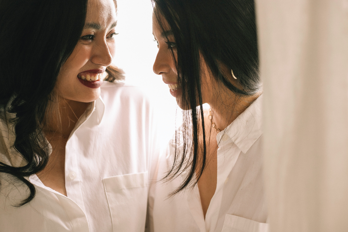 Two Asian women with long, black hair stare at each other, smiling