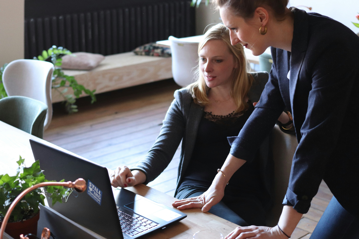 Two women engage in professionalism while they browse files on a computer at work.