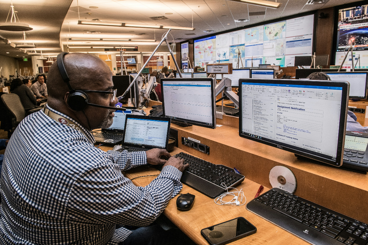 A Black man wearing a headset sits at a desk answering emergency calls for crisis management